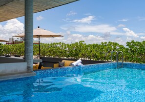 Zona de piscina con sillones, sombrillas y una vista despejada del cielo.