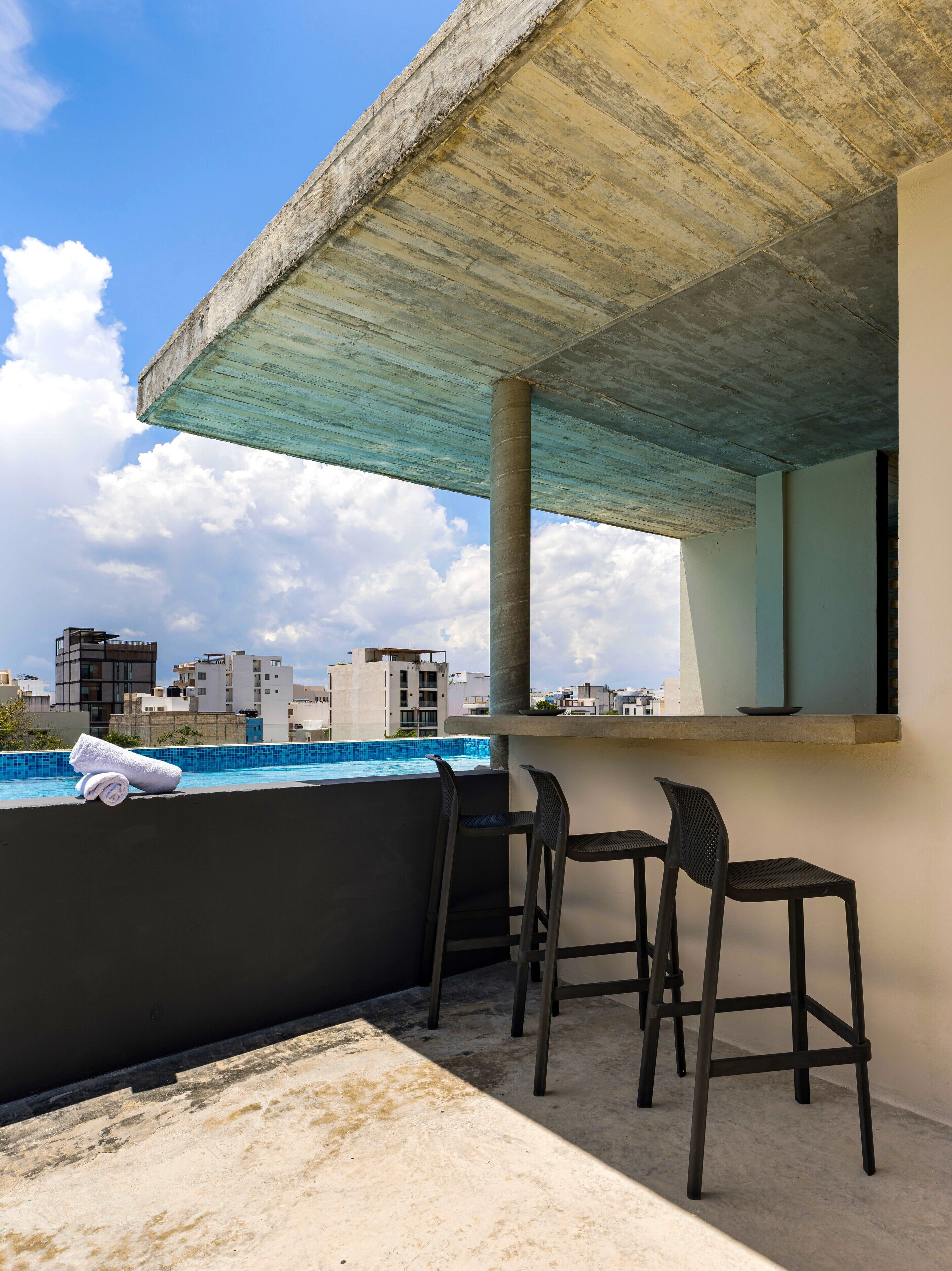 A rooftop terrace with a pool, three chairs, and a towel.
