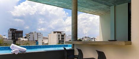A rooftop terrace with a pool, three chairs, and a towel.