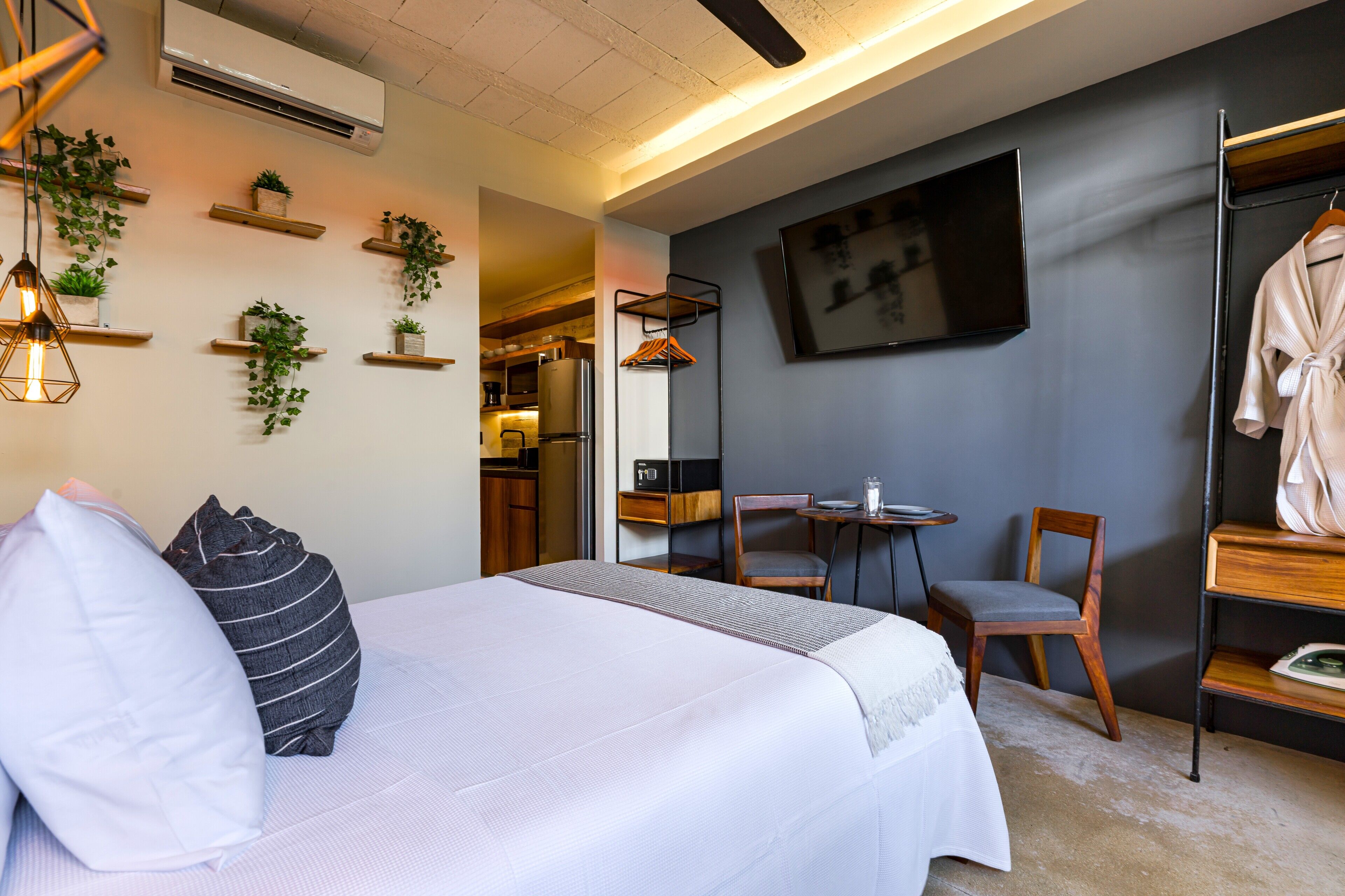 Una habitación de hotel moderna con cama, mesitas de noche, televisor, bata y un área de descanso con sillas y una mesa.