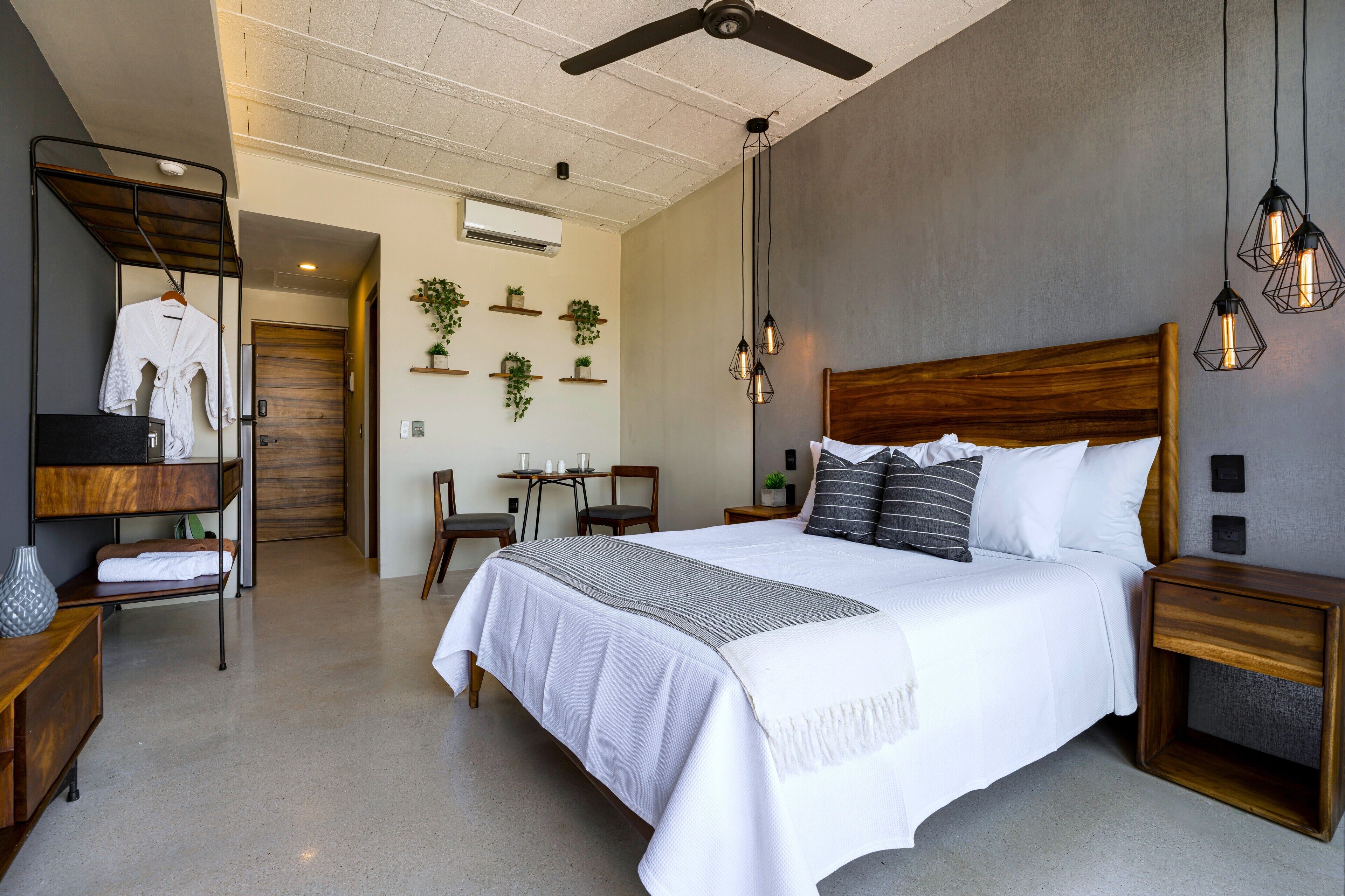 A modern hotel room with a large bed, wooden headboard, bedside tables, a wardrobe, a desk, and a ceiling fan.