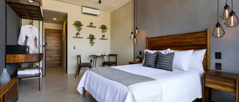 A modern hotel room with a large bed, wooden headboard, bedside tables, a wardrobe, a desk, and a ceiling fan.