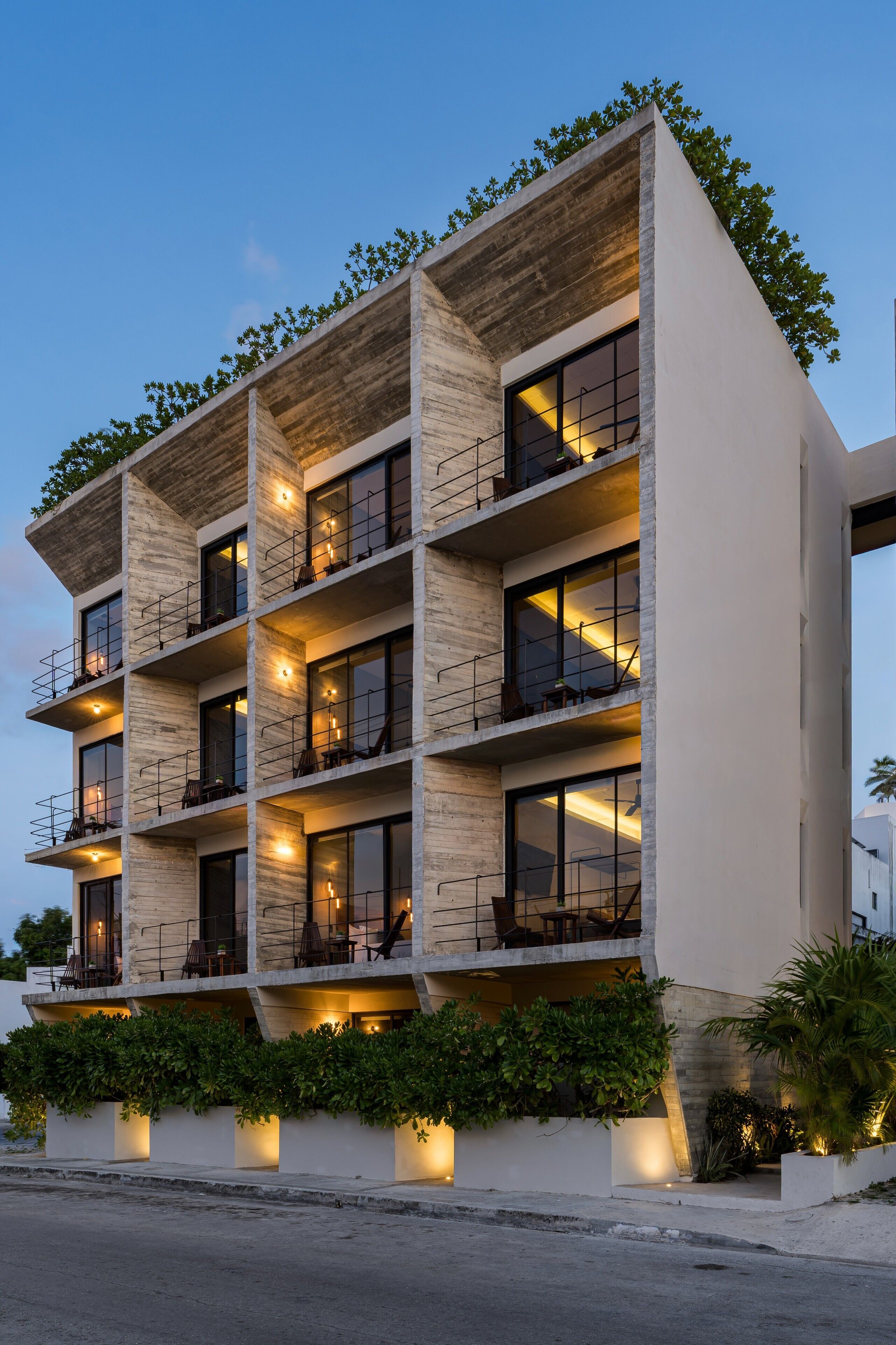 A modern multi-story building with balconies, large windows, and outdoor lighting.