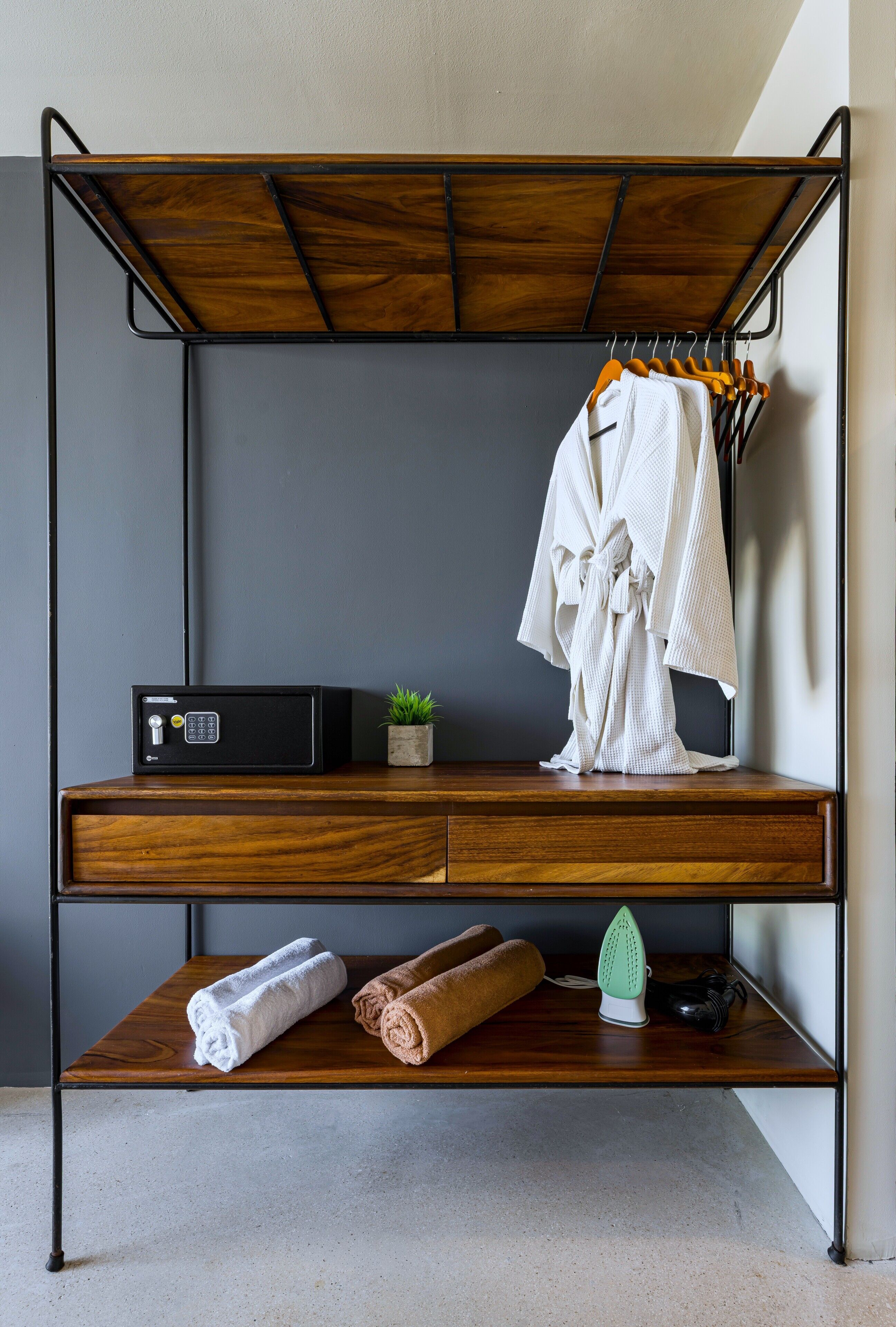 Une chambre compacte et moderne, dotée d’un bureau en bois, d’une petite plante en pot, d’une serviette et d’un fer à repasser.