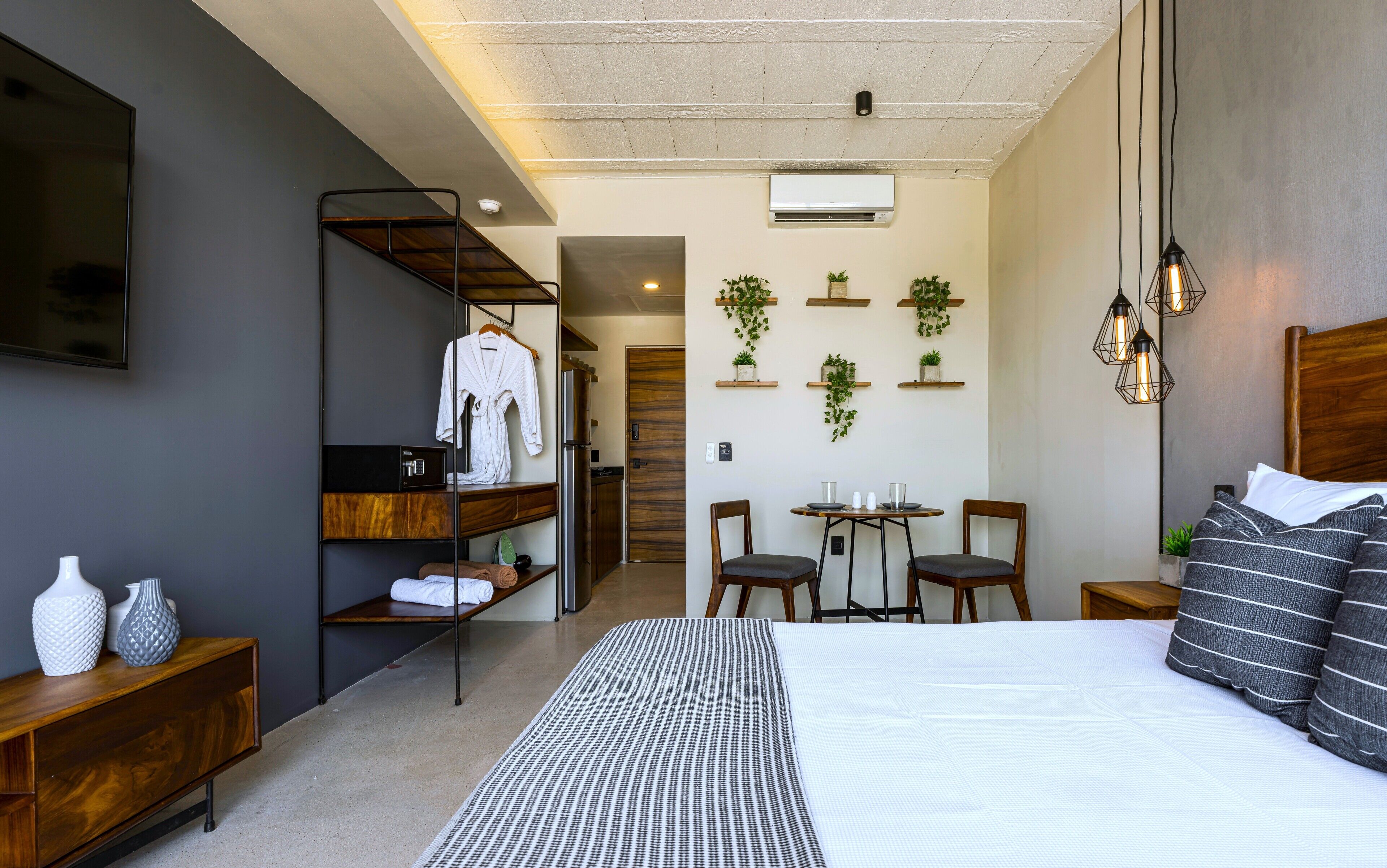 Ein modernes Hotelzimmer mit einem großen Bett, einem Fernseher, einem Schreibtisch mit Stühlen und einem kleinen Tisch mit Topfpflanzen.
