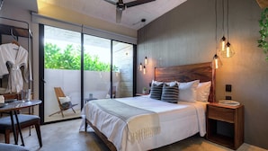 Ein Schlafzimmer mit einem großen Bett, einem Holzkopfende, Nachttischen, einem Sessel, einem Tisch mit einem Glas und einem Deckenventilator.