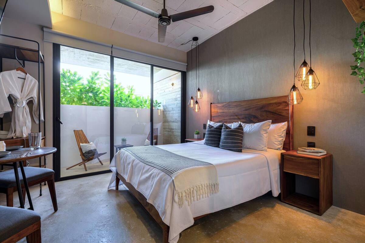 A bedroom with a large bed, a wooden headboard, bedside tables, a chair, a table with a glass, and a ceiling fan.