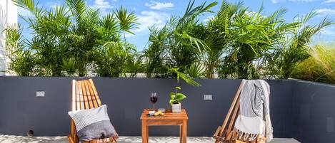 Dos sillones de madera, una mesita con una copa de vino y una planta en maceta.