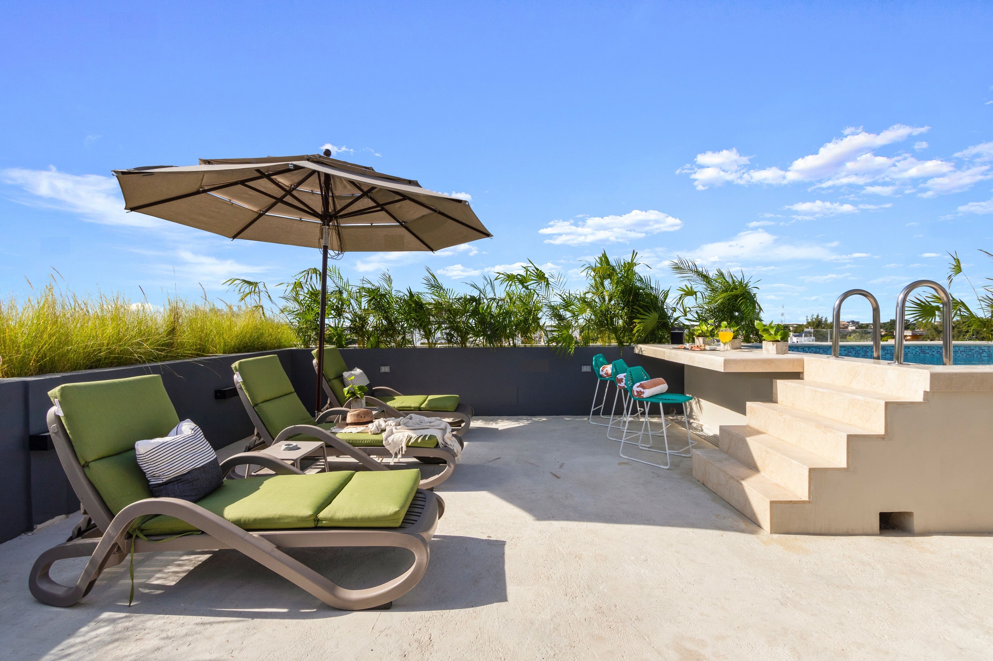 Zona de piscina en la azotea con sillones, una mesa y una sombrilla.