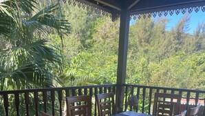 Een houten eettafel met zes stoelen, geplaatst op een betegelde vloer onder een overdekt terras met een balustrade.