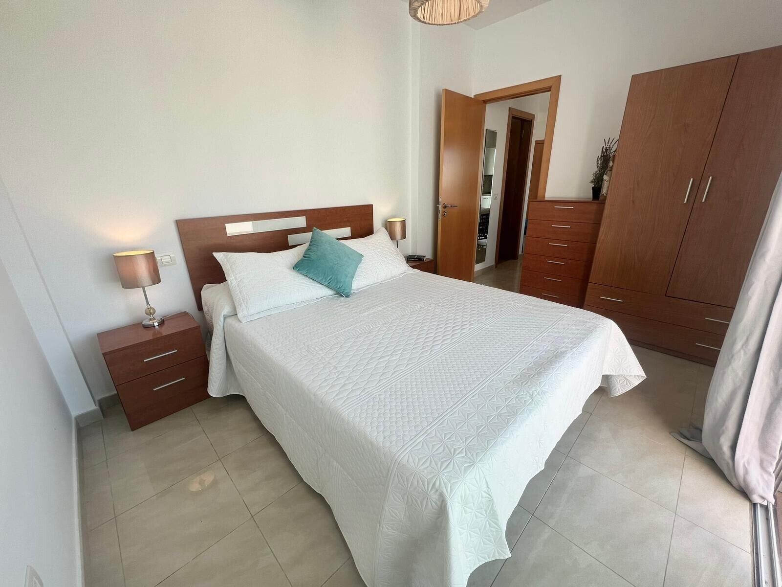 Een slaapkamer met een bed, nachtkastjes, een kledingkast en een deur naar een andere kamer.