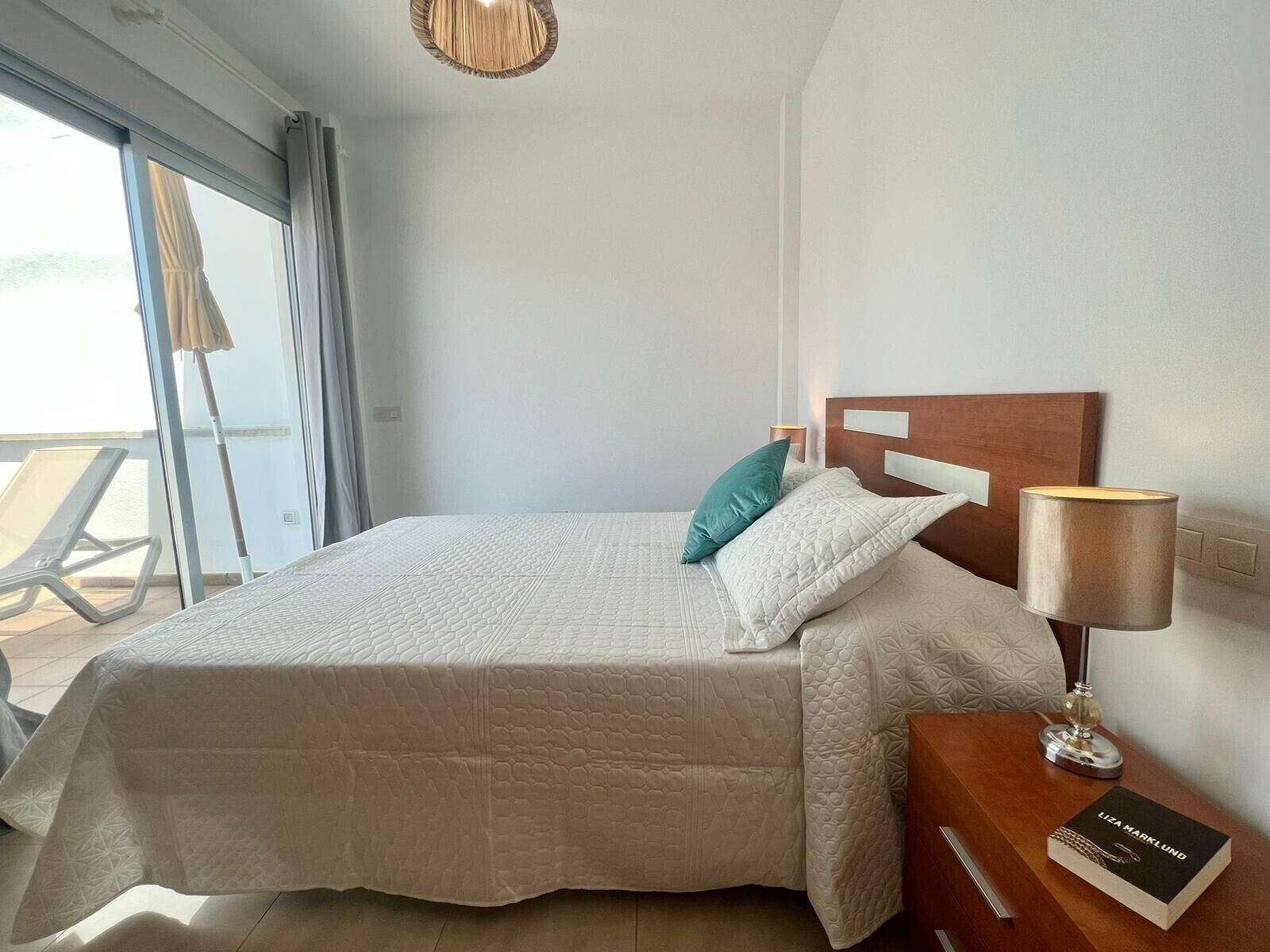 A neatly made bed with a headboard, a bedside lamp, and a book on a nightstand.