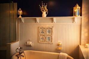 Un baño con bañera, tocador, espejo, repisa decorada y pared con cuadros.