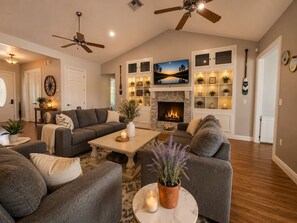 Ein großzügiges Wohnzimmer mit Kamin, zwei Sofas, einem Couchtisch und Deckenventilatoren.
