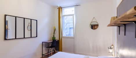 A hotel room with a bed, a desk, a chair, a window, and a mirror on the wall.