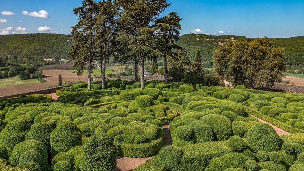 Ein angelegter Garten mit ordentlich geschnittenen Hecken, hohen Bäumen und freiem Blick auf die umliegende Landschaft.