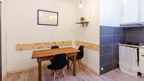 Ein Essbereich mit Holztisch und Stühlen, einer Weltkarte an der Wand, einem Regal mit einer Pflanze und einer Küche mit Herd und gefliestem Spritzschutz.