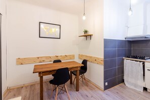 A dining area with a wooden table and chairs, a world map on the wall, a shelf with a plant, and a kitchen with a stove and tiled backsplash. - Central and Functional Apartment - Sarlat (Sarlat)