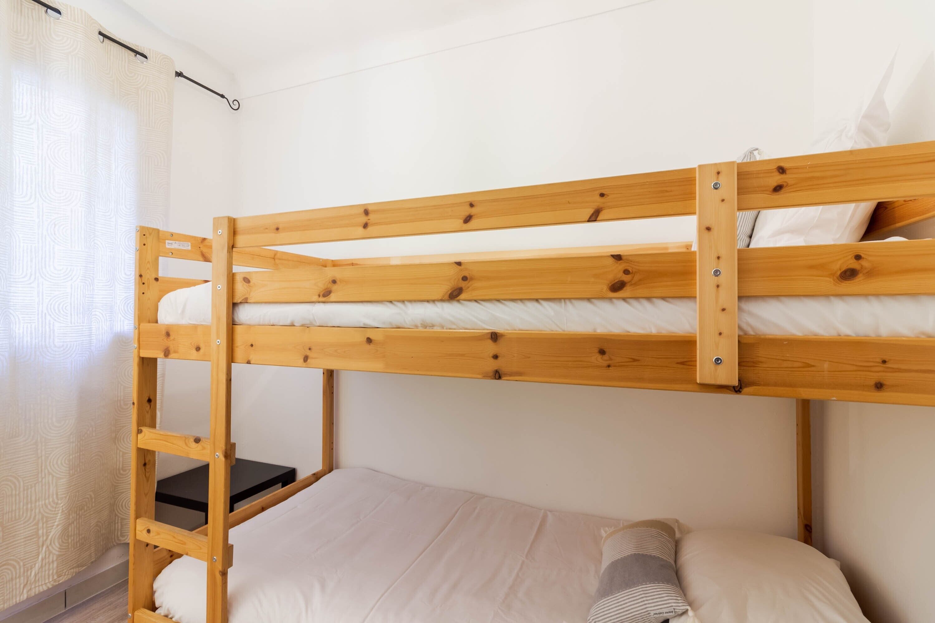A bunk bed with a ladder, a single bed below, and a curtain on the left.