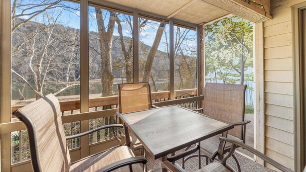 A covered patio with a table and chairs, large windows offering a view of trees and hills. - Water's Edge Hideaway – 6ppl (Branson)