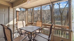 A covered patio with a table and chairs, large windows, and a view of trees and a lake. - Water's Edge Hideaway – 6ppl (Branson)