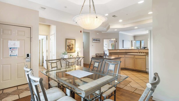 A dining area with a glass table and chairs, a chandelier, and a kitchen in the background. - Golf View Getaway – For 6 (Branson)