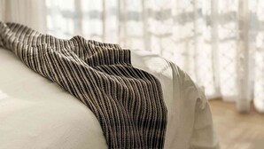Una cama con un edredón a rayas y cortinas traslúcidas en una habitación con suelo de madera.