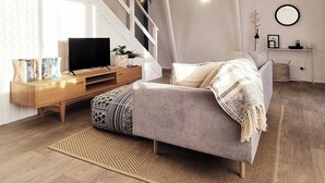 Una sala moderna con un sofá gris, mueble de entretenimiento de madera y una escalera.