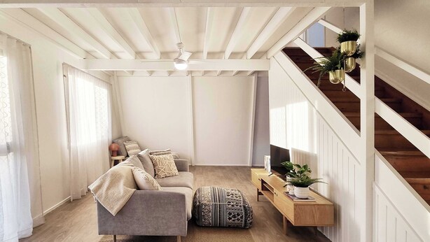 Una sala de estar moderna con un sofá gris, un taburete estampado, una consola de madera y una escalera con barandilla.