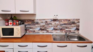 Een keuken met witte kasten, een magnetron, een spoelbak en een achterwand van steen.