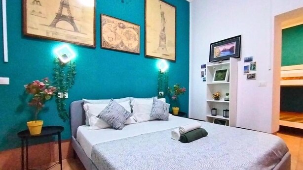 Een netjes ingerichte slaapkamer met een bed, een klein tafeltje met een plant in pot en een muur met ingelijste foto's.