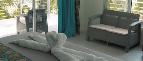 A room with a bed, a sofa, and a chair. There is a view of greenery outside the window.