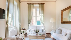 A well-lit living room with a white sofa, a coffee table, and a dining area with a table set for two. - Bright and Central Apartment in Lucca (Lucca)