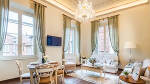 A spacious living room with a chandelier, a white sofa, a dining table set for four, and a television mounted on the wall. - Bright and Central Apartment in Lucca (Lucca)