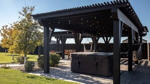 En overdækket terrasse med boblebad, træmøbler og et pergola.