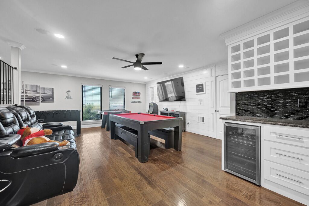 A modern living room with a pool table, leather sofa, and a television mounted above a kitchen area.