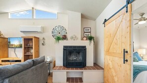 A living room with a fireplace, a sofa, a wooden cabinet, and a sliding barn door. - Private Guesthouse w/ Pool in Historic Wickenburg! (Wickenburg)