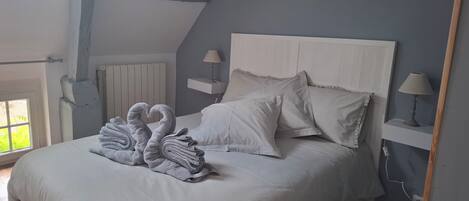 A bedroom with a bed, two bedside tables with lamps, a radiator, and a window with a view of greenery.