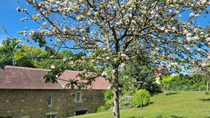 Un bâtiment en pierre doté d’un toit en pente, entouré d’une pelouse et d’arbres en fleurs.