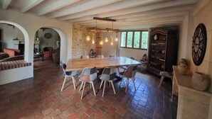 Un vaste espace dédié à la salle à manger, avec une grande table en bois et des chaises modernes, un mur en pierre et un buffet en bois rustique où sont rangés la vaisselle.