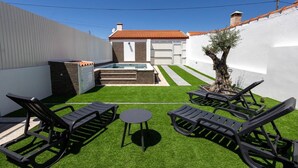 Un jardin avec une pelouse artificielle, un jacuzzi et du mobilier d’extérieur.
