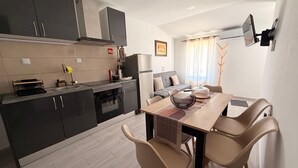 Une cuisine moderne avec des meubles de rangement aux couleurs foncées, une table à manger avec des chaises et un coin salon comprenant un canapé et un téléviseur.