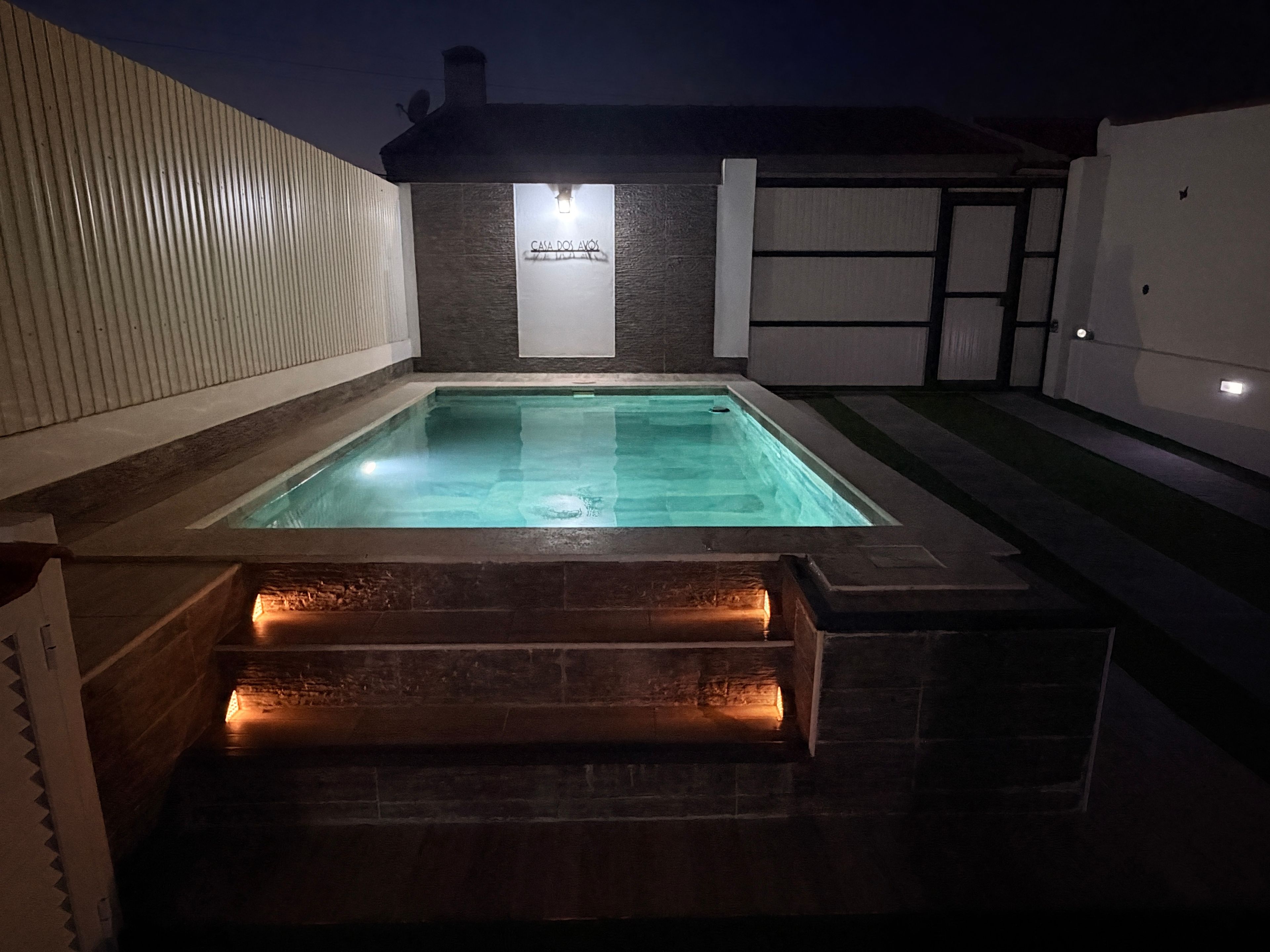 A rectangular swimming pool with a stone border and a small waterfall feature at the bottom.