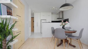 A modern kitchen with white cabinets, a central island, and a dining area with grey chairs and a wooden table. - Stylish Apartment in the Center | Balcony | Workspace (Warszawa)