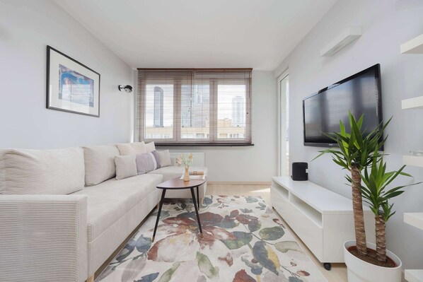 Una sala de estar moderna con un sofá, una mesita, una planta en maceta, un televisor de pantalla plana y una ventana con persianas.