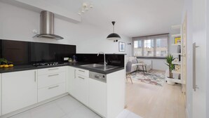 A modern kitchen with white cabinets, a black countertop, stainless steel range hood, and a black pendant light. - Stylish Apartment in the Center | Balcony | Workspace (Warszawa)
