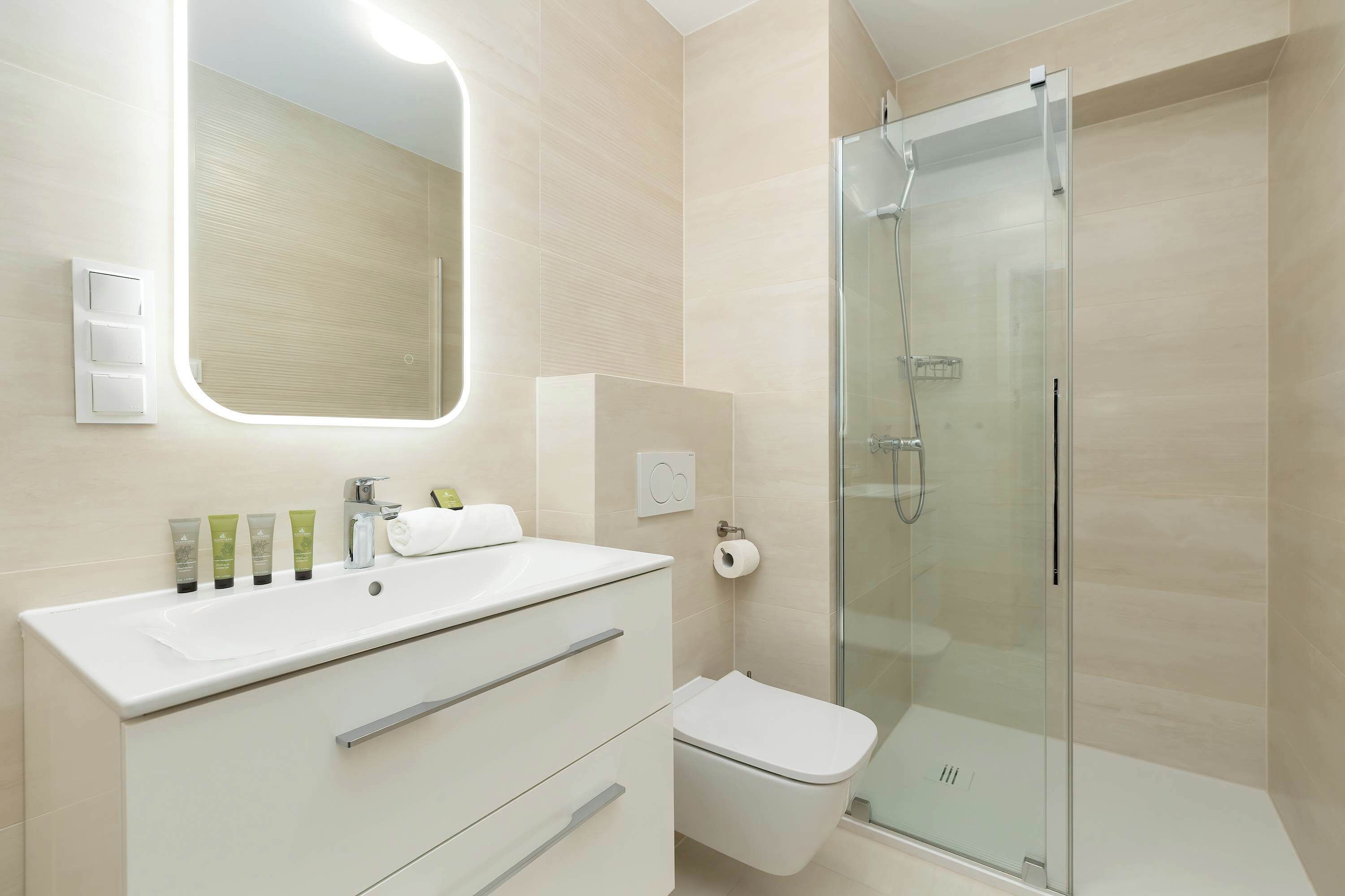 A modern bathroom with a large mirror, a white sink, a glass shower enclosure, and a toilet.