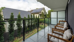 A balcony with a glass railing, wooden chairs, and a view of neighboring houses and trees.