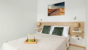 A bedroom with a bed, a nightstand, a wall-mounted lamp, and a painting of a desert landscape.