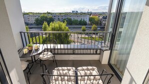 Ein Balkon mit Tisch, zwei gepolsterten Stühlen, einem kleinen Topfpflanzen und Blick auf einen Parkplatz und Gebäude.